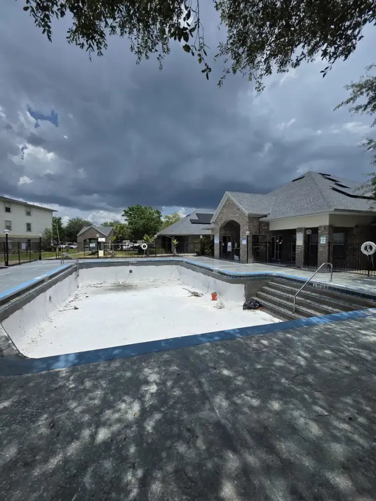 Drained community swimming pool with a worn gray deck before surface restoration.