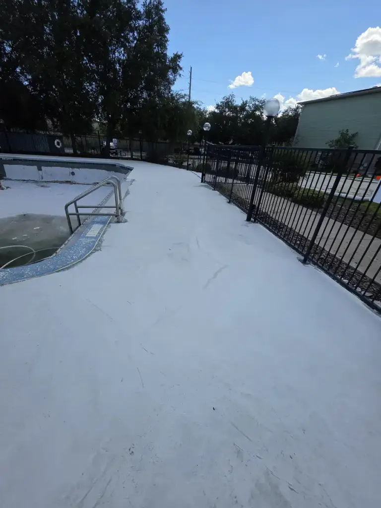 Community pool deck during a broad light-colored coating stage with the pool area closed for work.