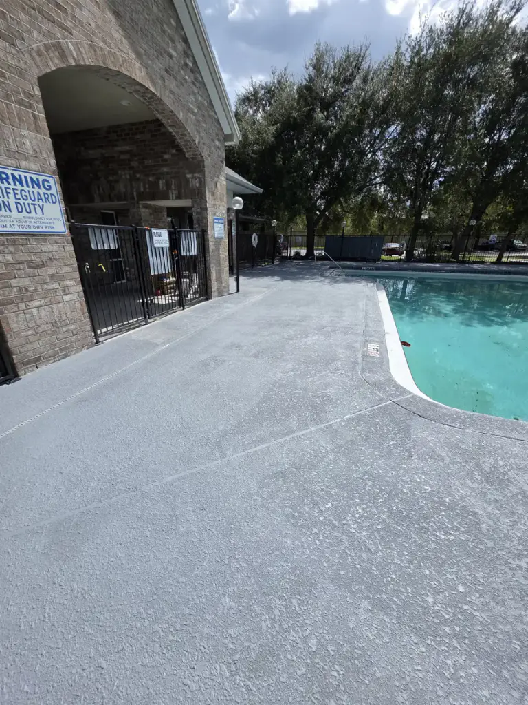Refilled community swimming pool beside a continuous finished gray deck after surface restoration.