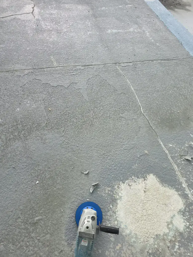 Hand grinder beside an opened section of deteriorated coating on a community pool deck.