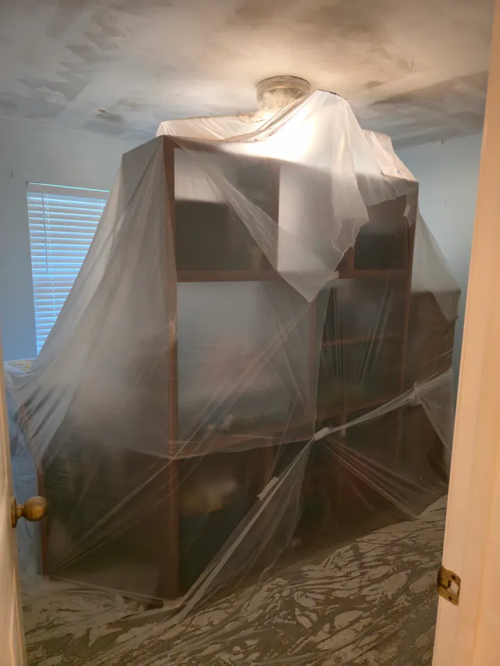 Furniture wrapped in plastic below an actively prepared ceiling.
