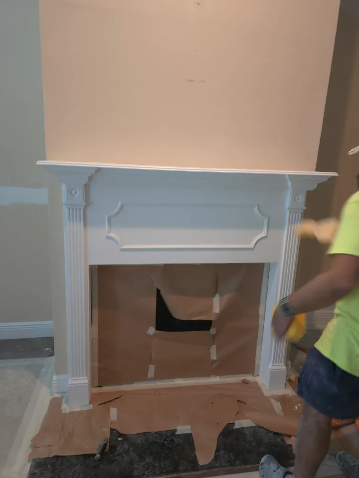 Fireplace surround and adjacent wall during active painting work.