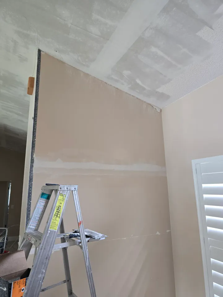 Large room with floor protection, ladders, and ceiling preparation in progress.