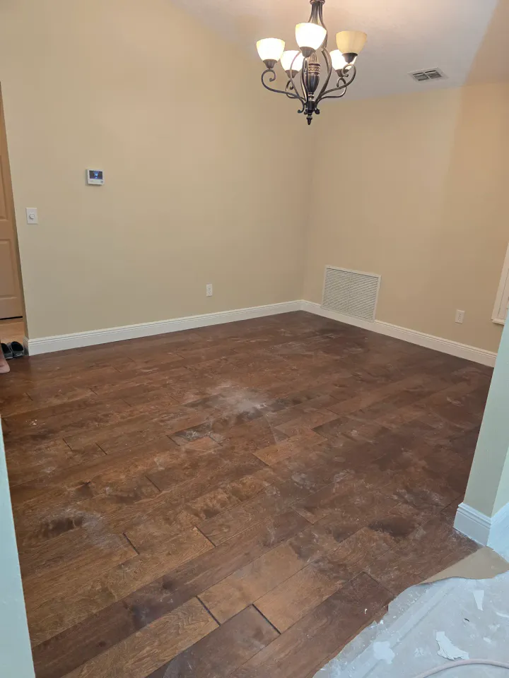 Dining area with neutral walls, white trim, dusty dark flooring, and an unfinished foreground threshold.
