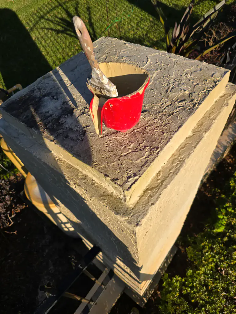 Paint cup and brush resting on the textured top of an exterior column during coating work
