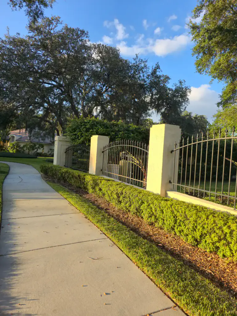 Light-colored textured columns and low wall along a black metal entry fence