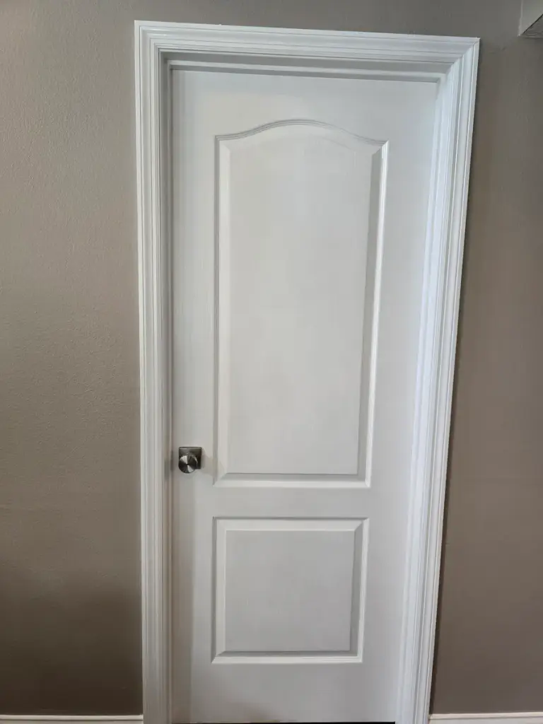 Finished white paneled interior door and casing against warm neutral walls