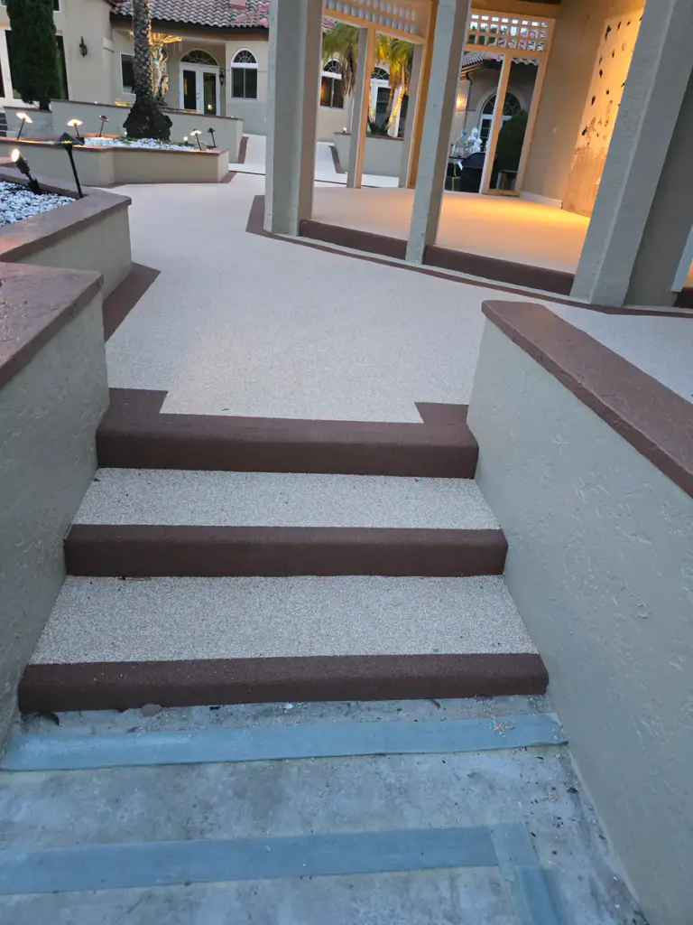 Finished light-tan landing and stair surfaces framed by dark accent borders, with a prepared gray pool-level area in the foreground.