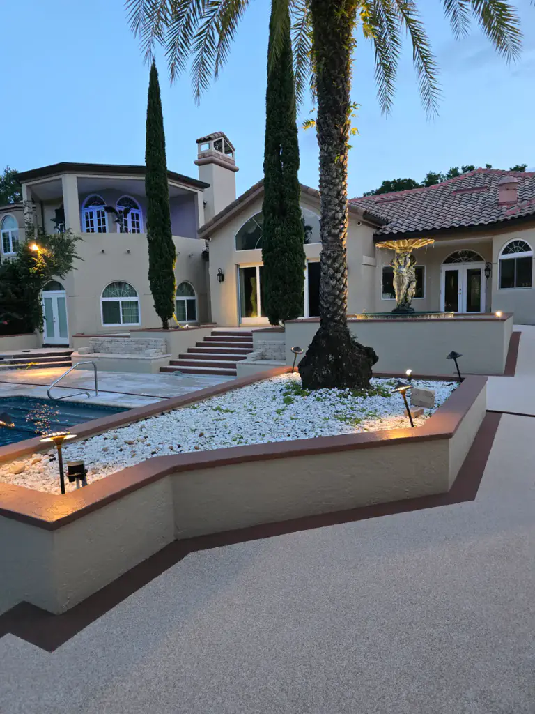 Wide dusk view of finished light-tan courtyard walkways and dark accent borders, with a gray prepared pool-level area visible at left.