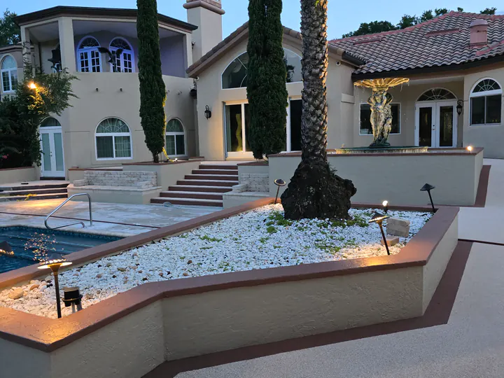 Wide dusk view of finished light-tan courtyard walkways and dark accent borders, with a gray prepared pool-level area visible at left.