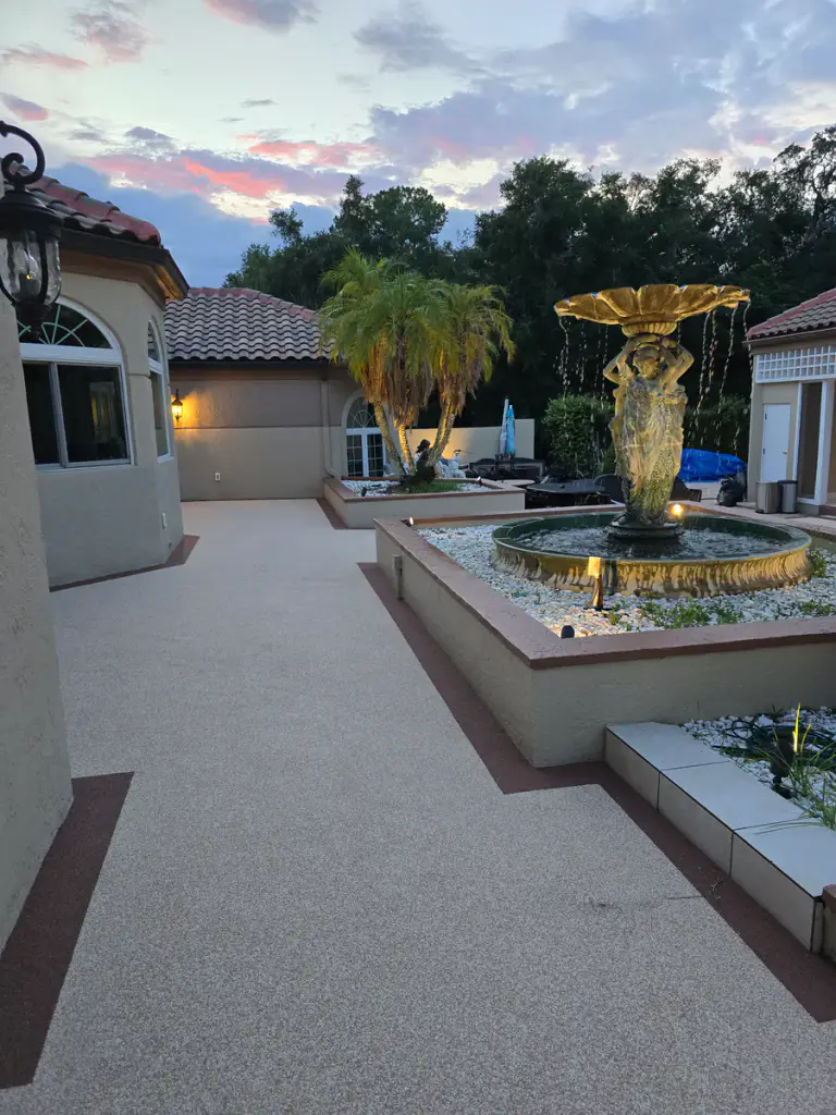 Finished light-tan courtyard walkway with dark accent borders around a raised fountain planter.