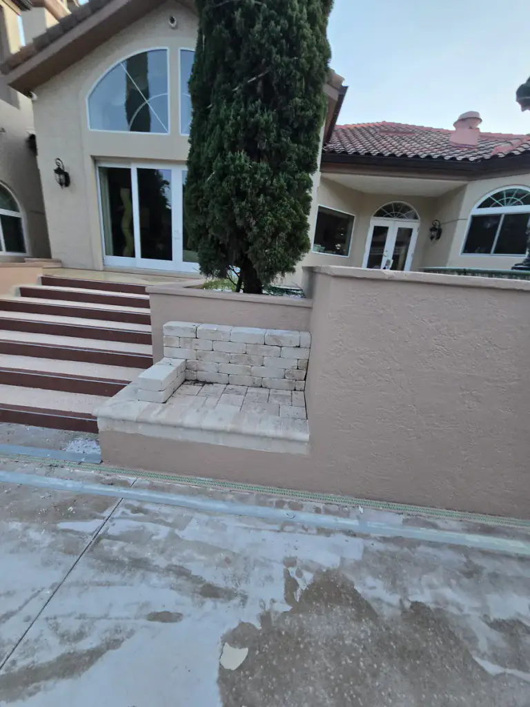 Prepared light-gray pool-deck area beside steps and raised courtyard walls.