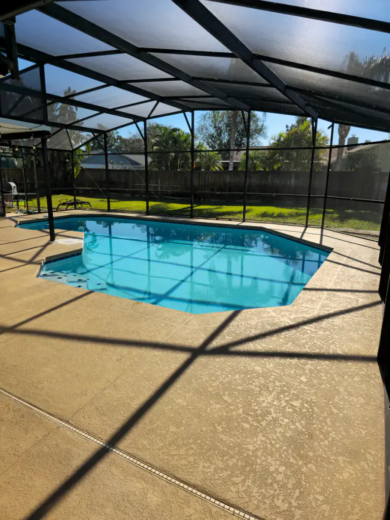 Completed light neutral pool-deck surface across the screened enclosure perimeter.