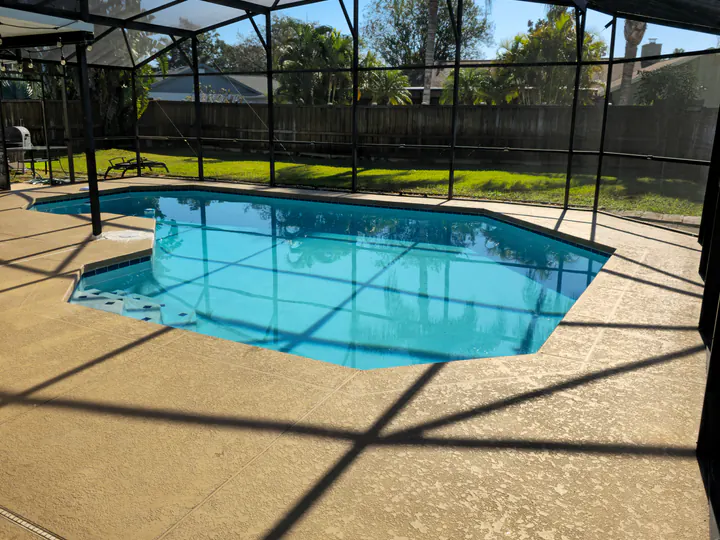 Completed light neutral pool-deck surface across the screened enclosure perimeter.