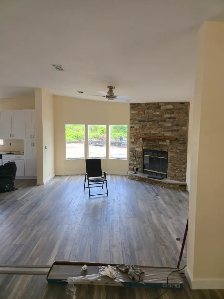 Open living area with installed flooring, light walls, a stone fireplace, and boxed materials.