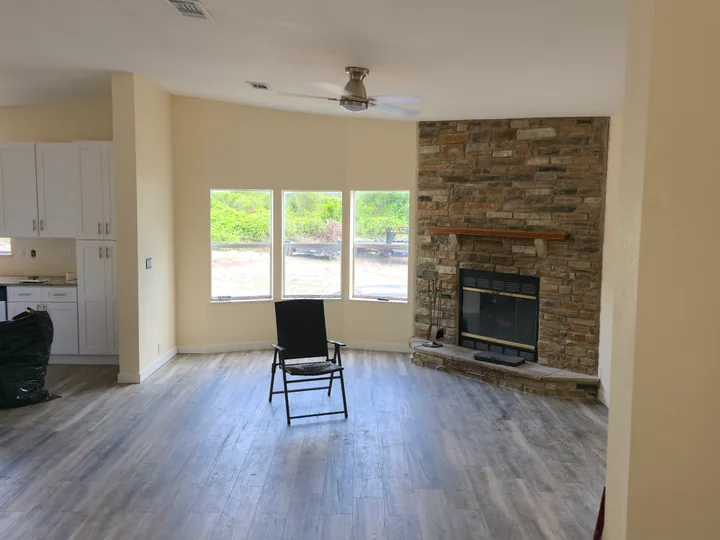 Open living area with installed flooring, light walls, a stone fireplace, and boxed materials.