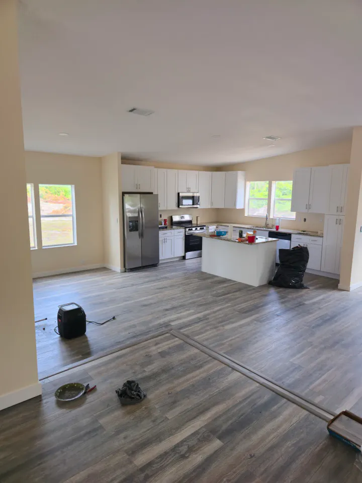 Open kitchen and living area with installed flooring, painted walls, tools, and protective materials.