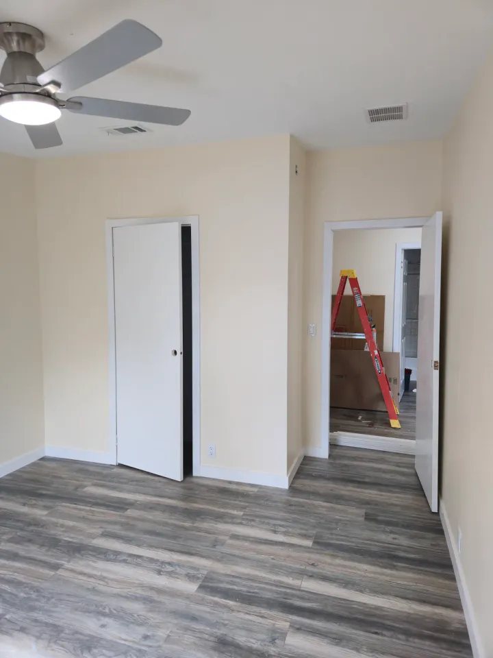 Interior doorway and adjoining rooms with plank flooring, a ladder, boxes, and an unfinished wall opening.