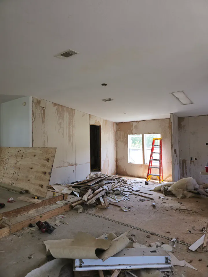 Interior room during demolition with stripped surfaces, debris, tools, and a ladder.
