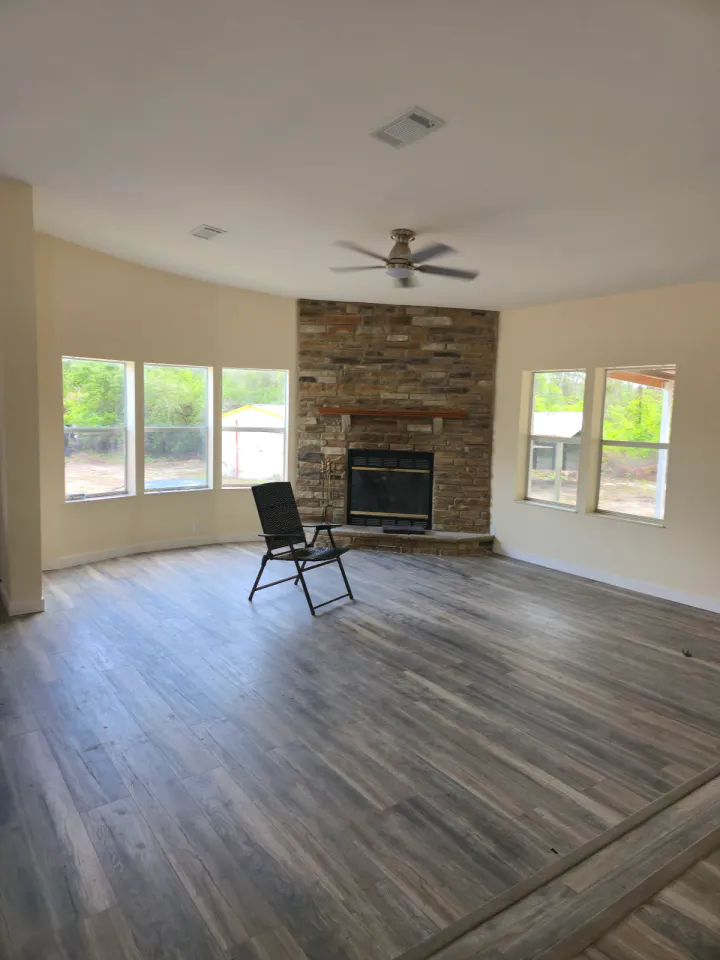Large living room with plank flooring, light walls, ceiling fixtures, and a stone fireplace.