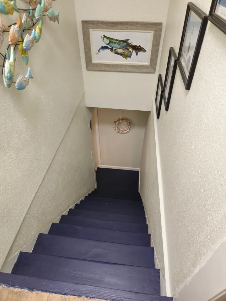 Dark stair treads viewed downward with light walls and a dark handrail.