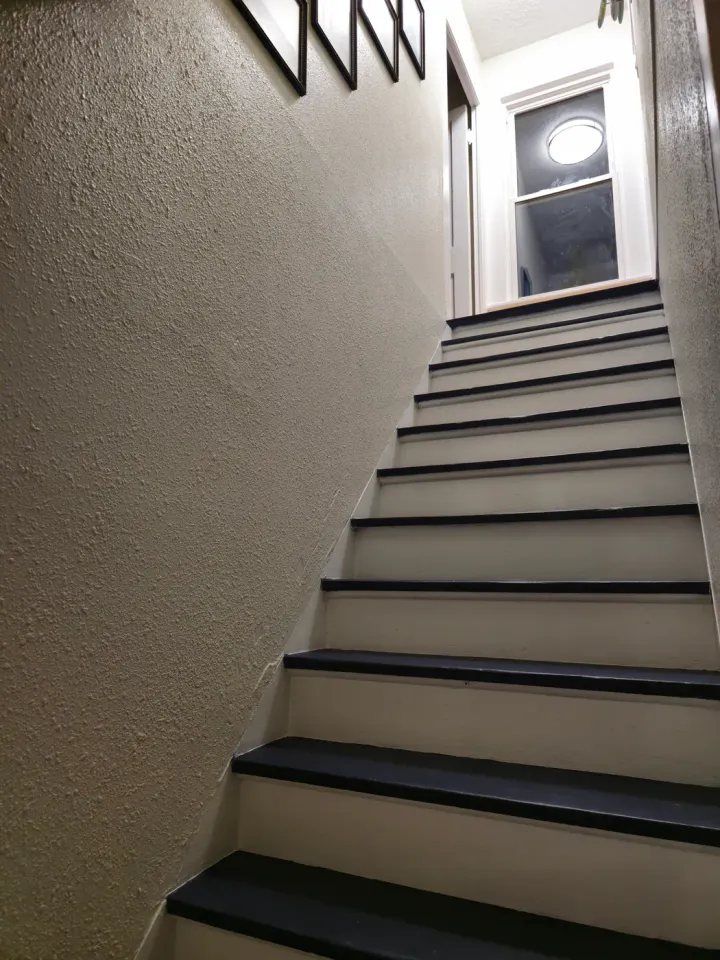 Dark stair treads viewed upward between light walls with framed wall decor.