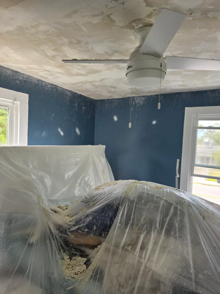 Interior room with furniture wrapped in plastic while ceiling preparation is underway.